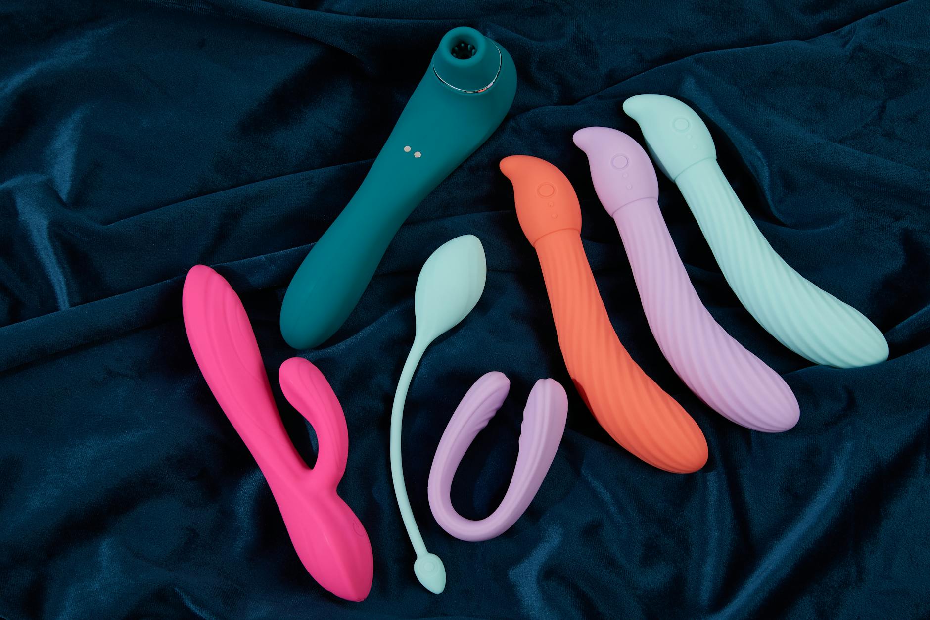 A teal silicone vibrator on smooth white silk, representing gentle post-recovery pleasure tools.