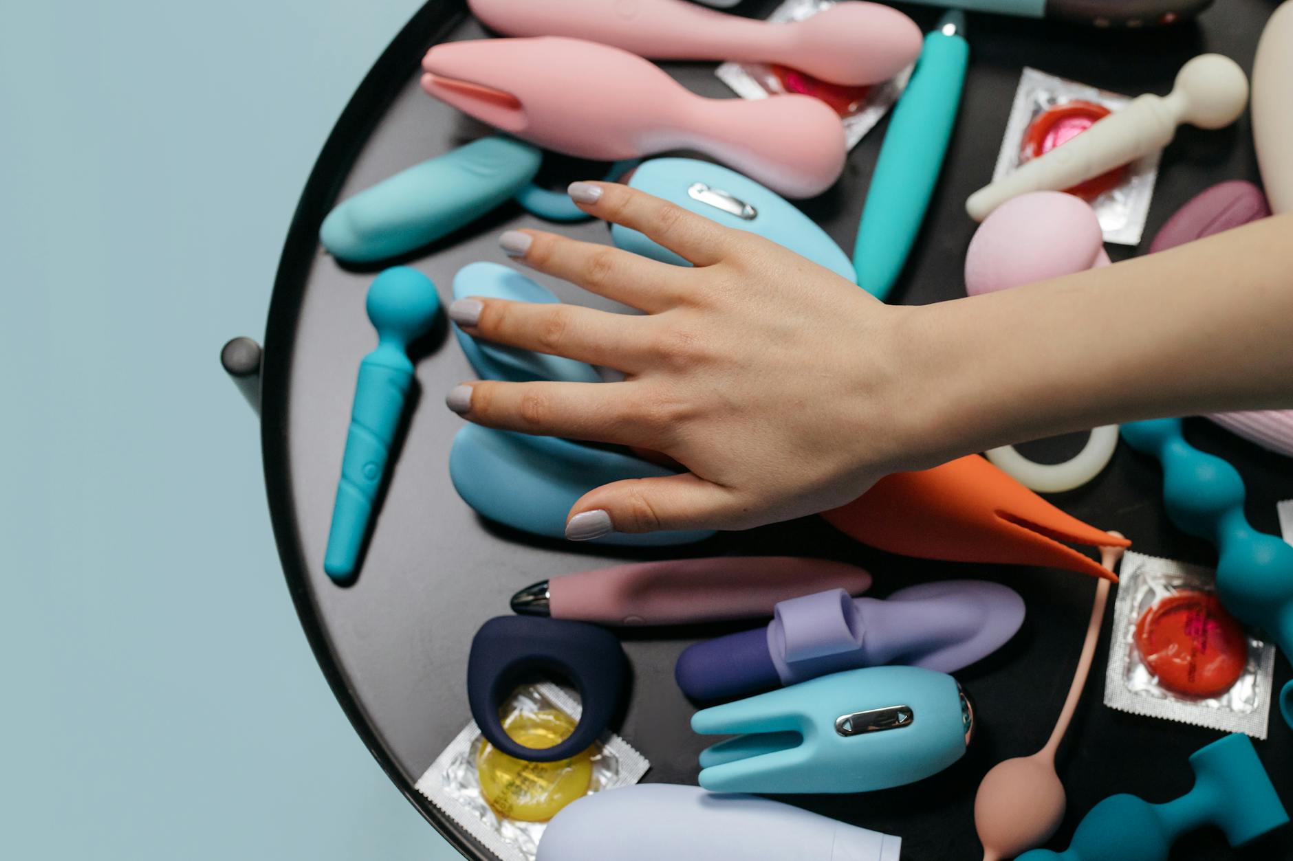 Hand reaching toward a variety of colorful silicone toys arranged on a table