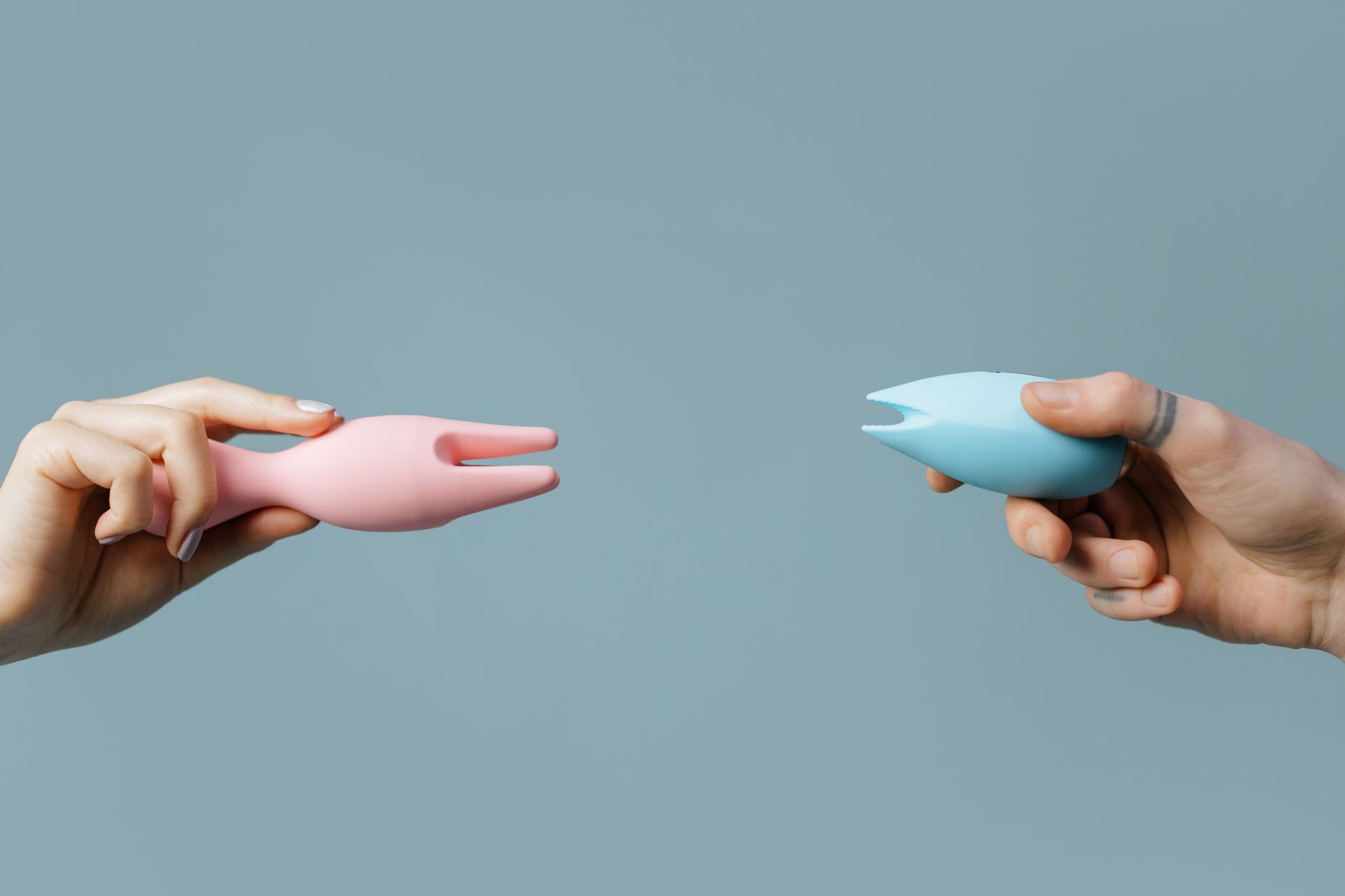 Woman holding blue and pink silicone vibrators in a thoughtful, contemplative manner