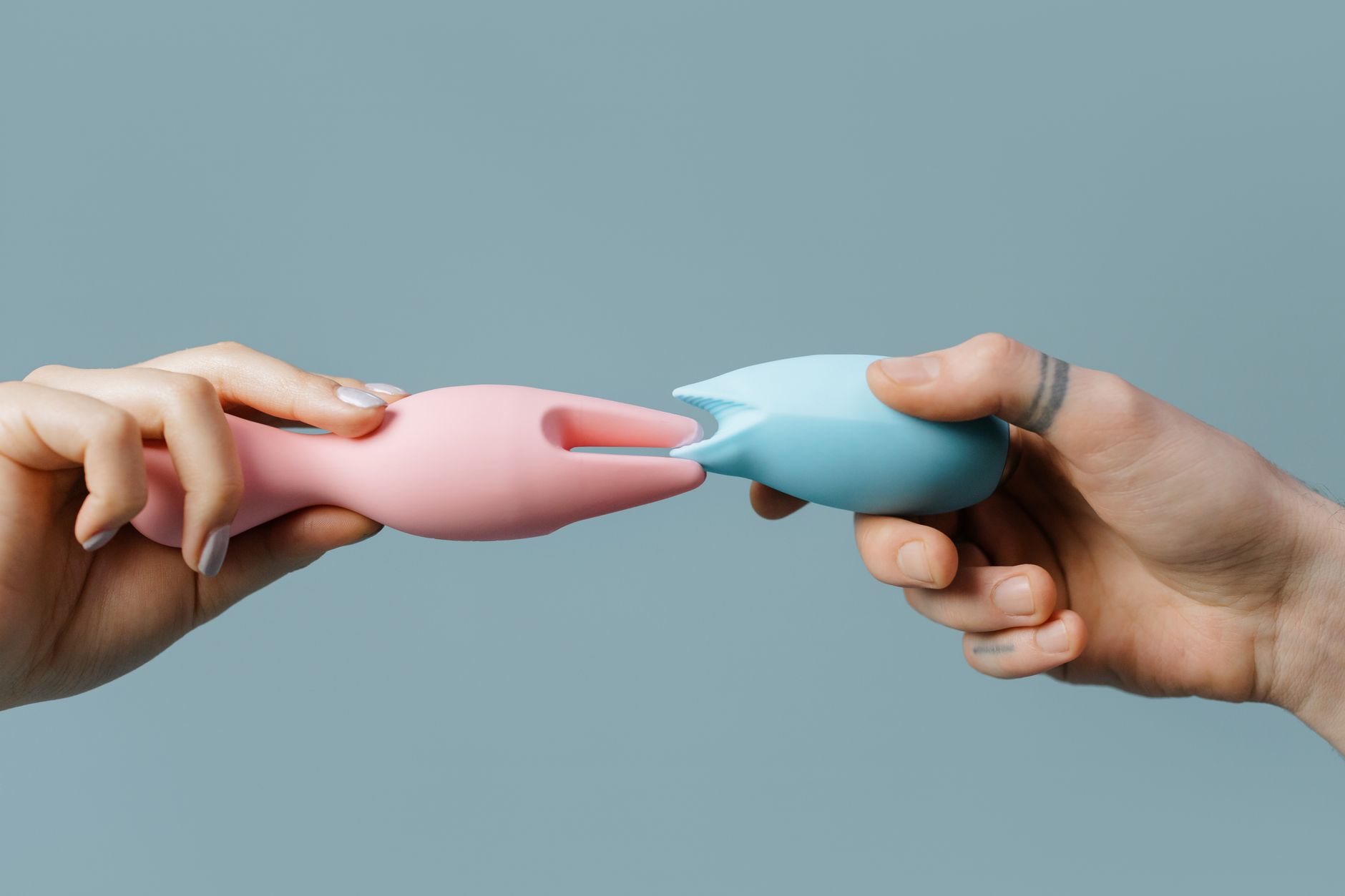 Hands holding pastel-colored silicone toys for intimate moments