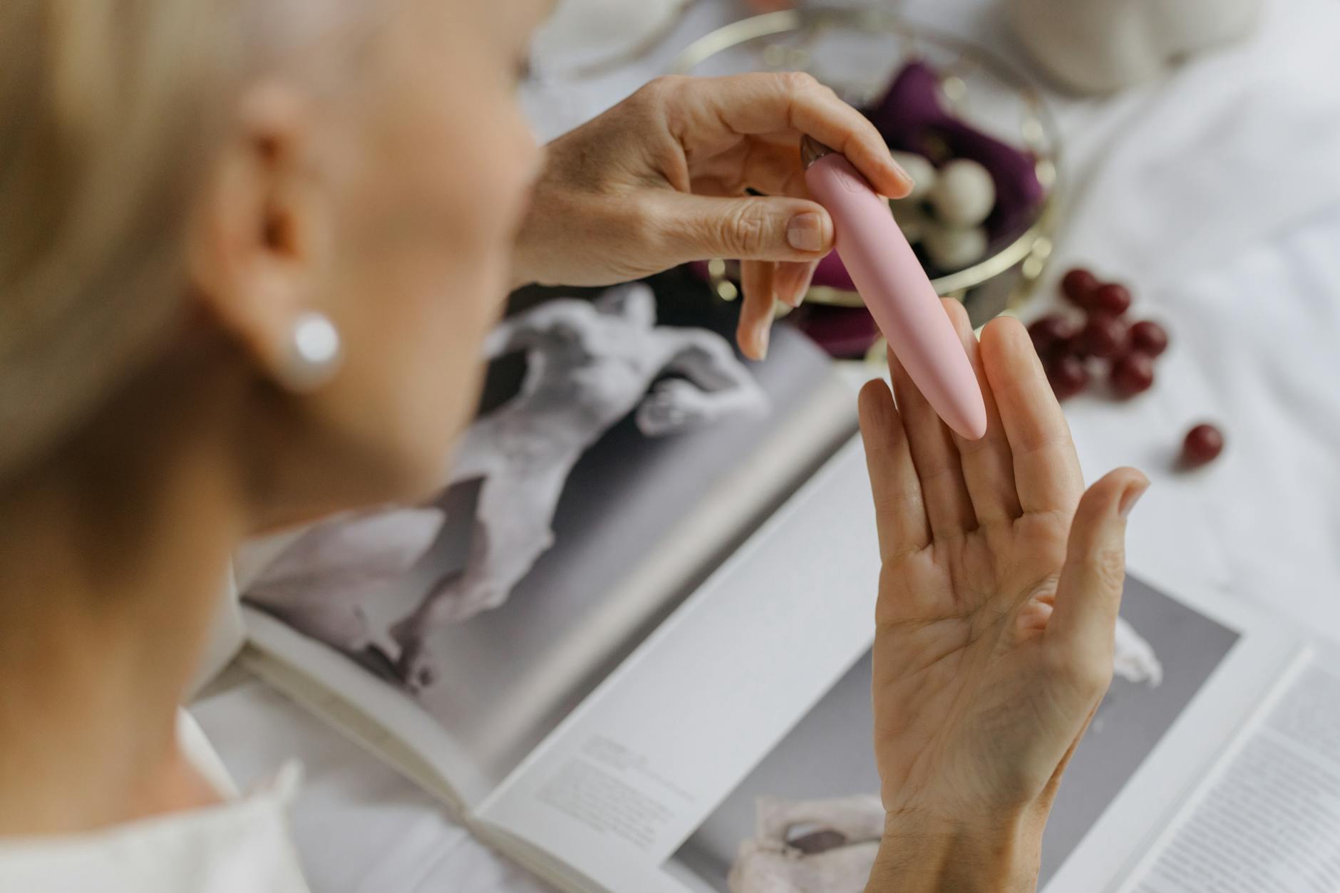 Close-up of a hand holding a pink vibrator with intimate personal items in soft focus background