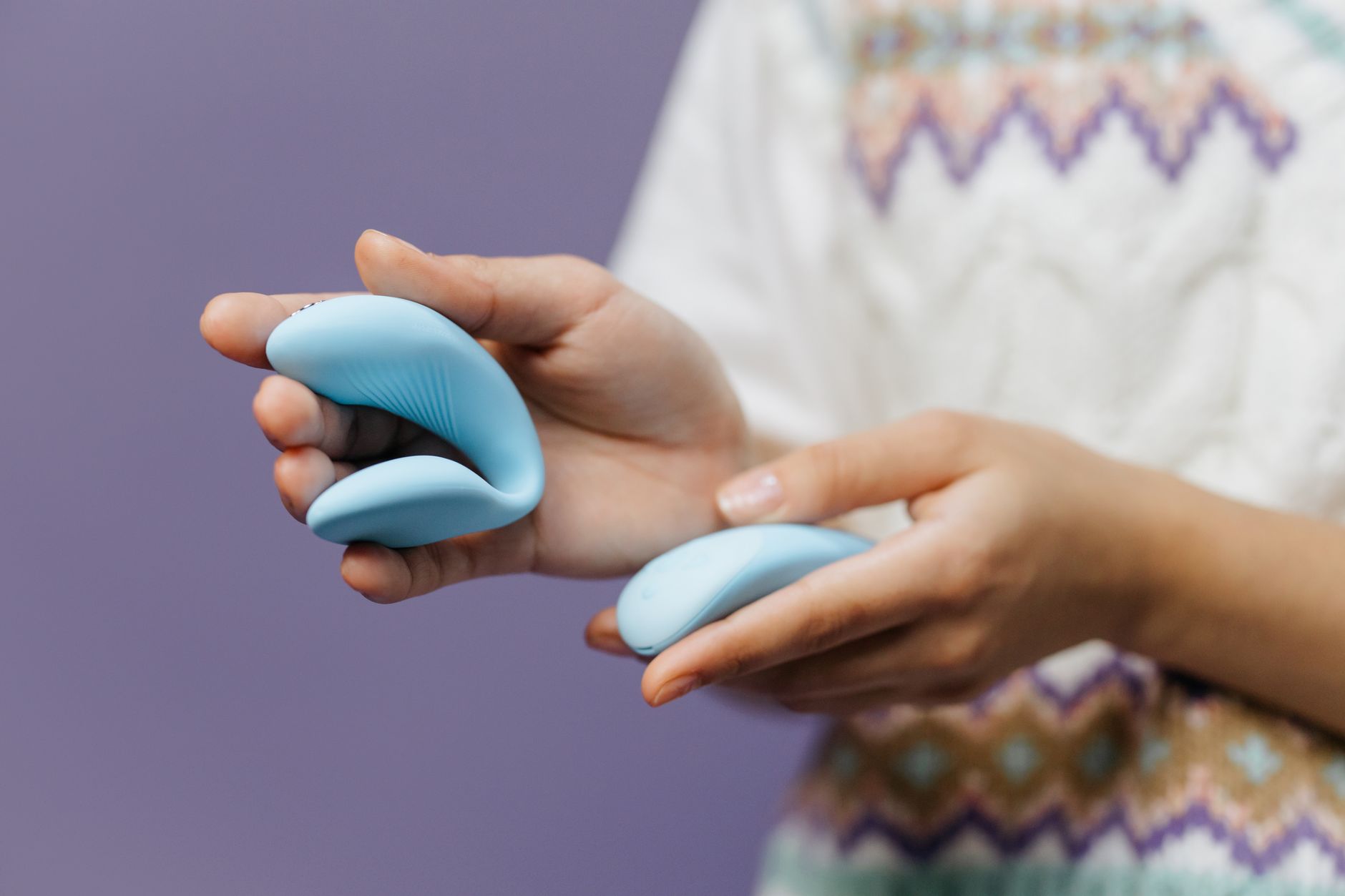 Hand holding a sleek blue lemon vibrator against a purple background