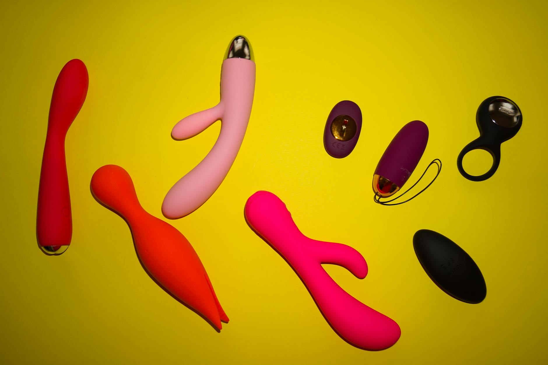 A hand reaching over a variety of colorful sex toys arranged on a table.