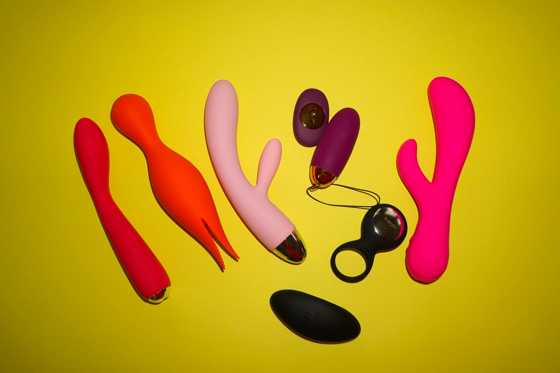 Colorful clitoral vibrators and adult toys arranged on a bright yellow surface